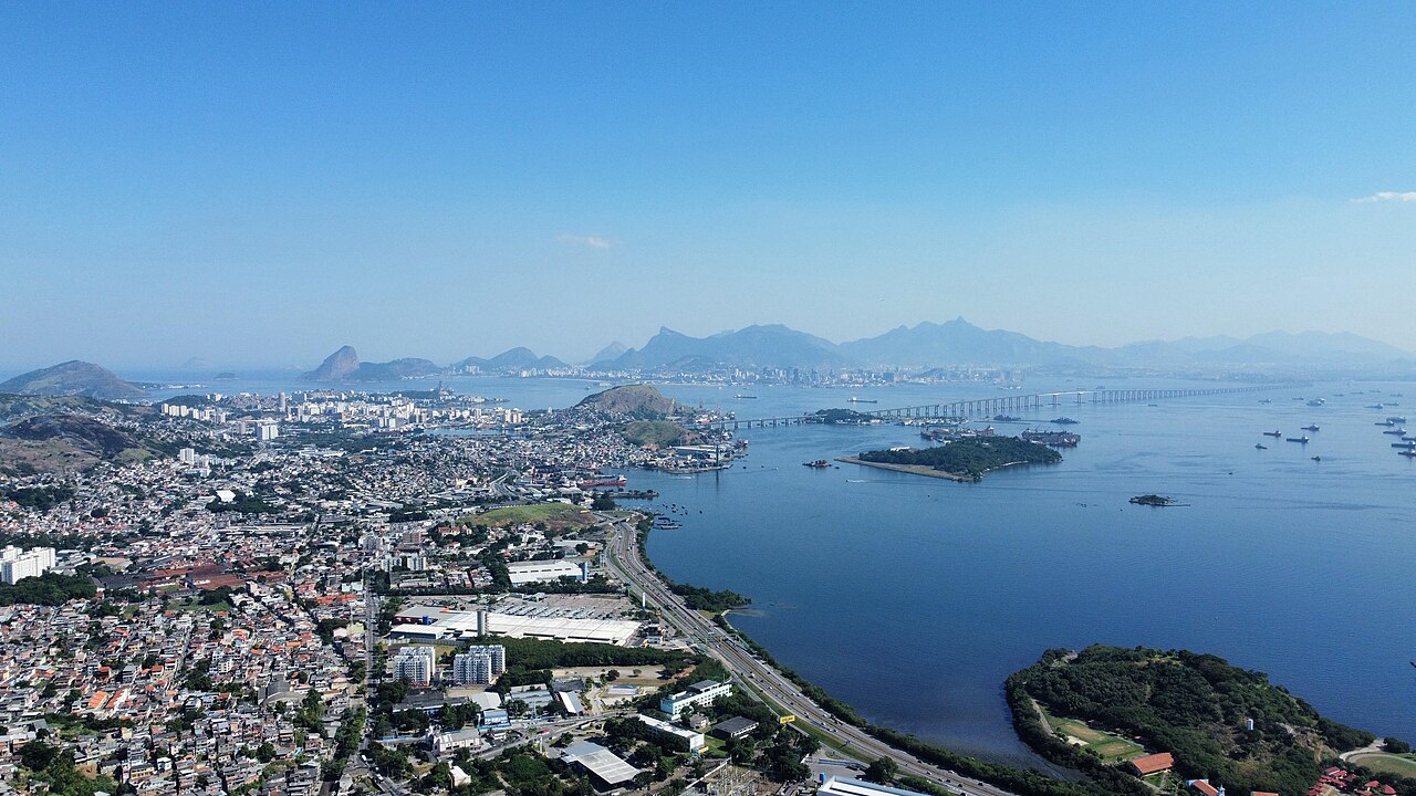 Vista aérea do bairro Neves, em São Gonçalo, Rio de Janeiro, com casas e prédios à esquerda, a Baía de Guanabara à direita e a Ponte Rio-Niterói e as montanhas do Rio ao fundo